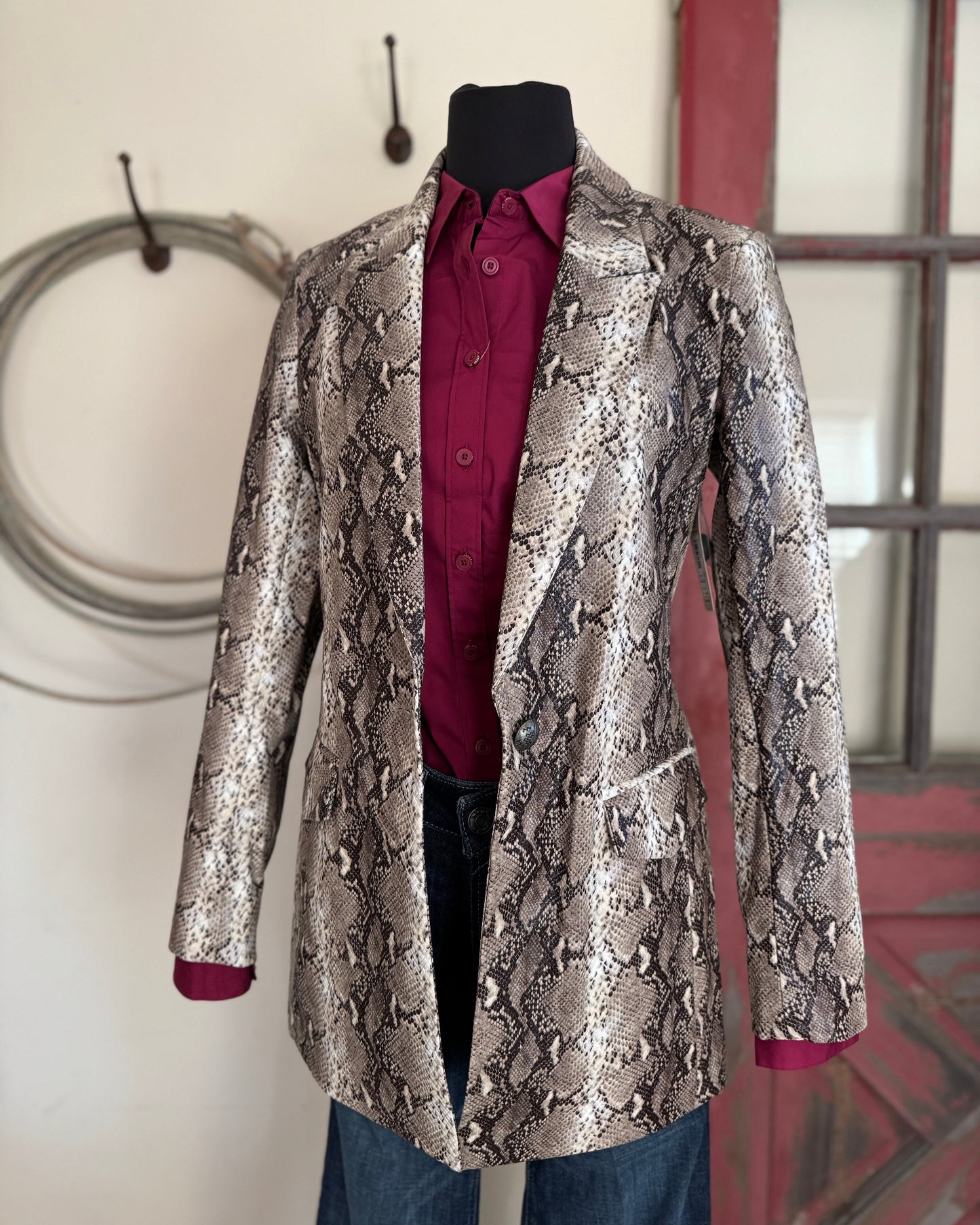 Patterned coat with a red shirt underneath on a mannequin against a neutral wall.