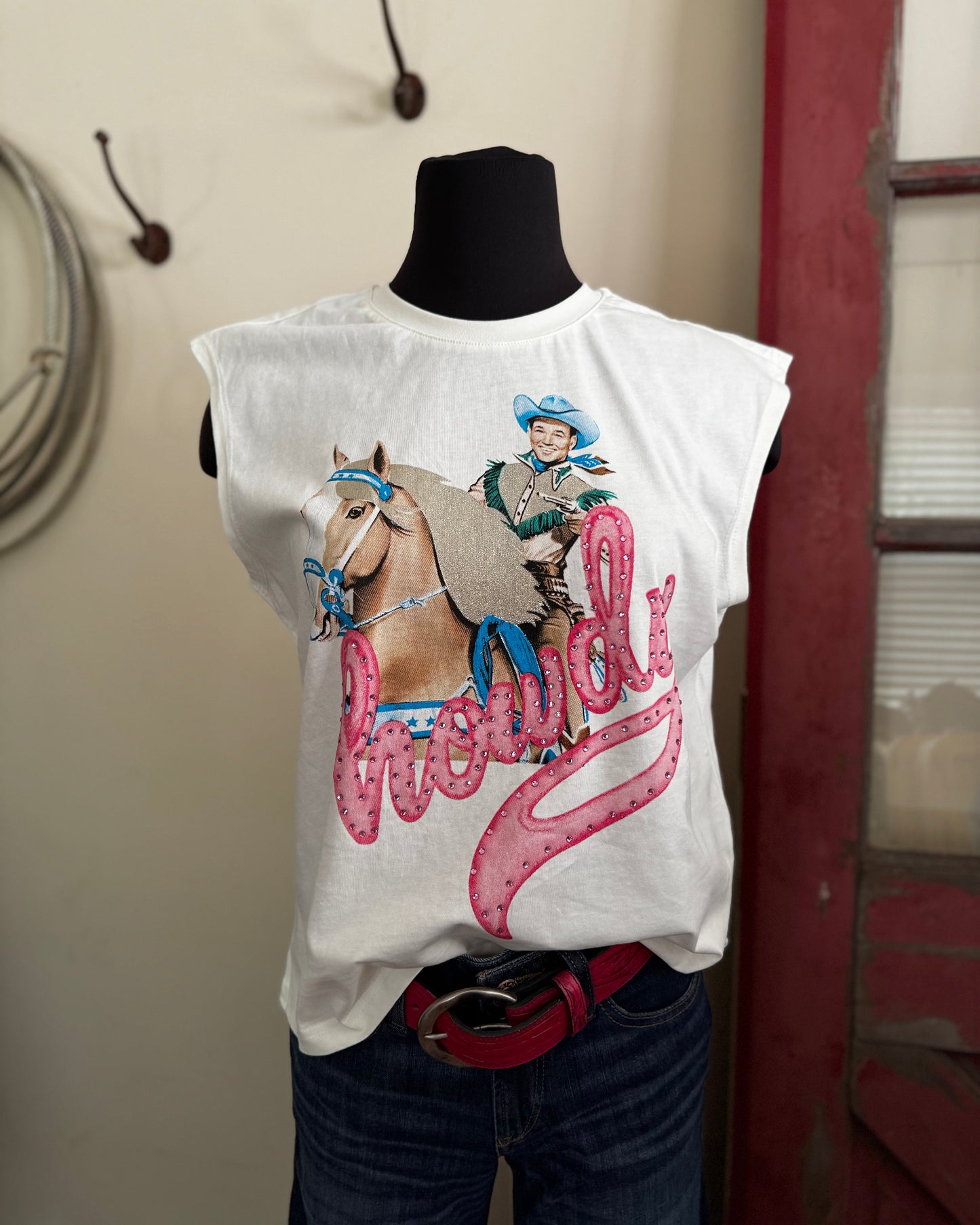 White sleeveless shirt with a graphic of a cowgirl on a horse and the word 'Chewy' displayed on a mannequin against a neutral wall.