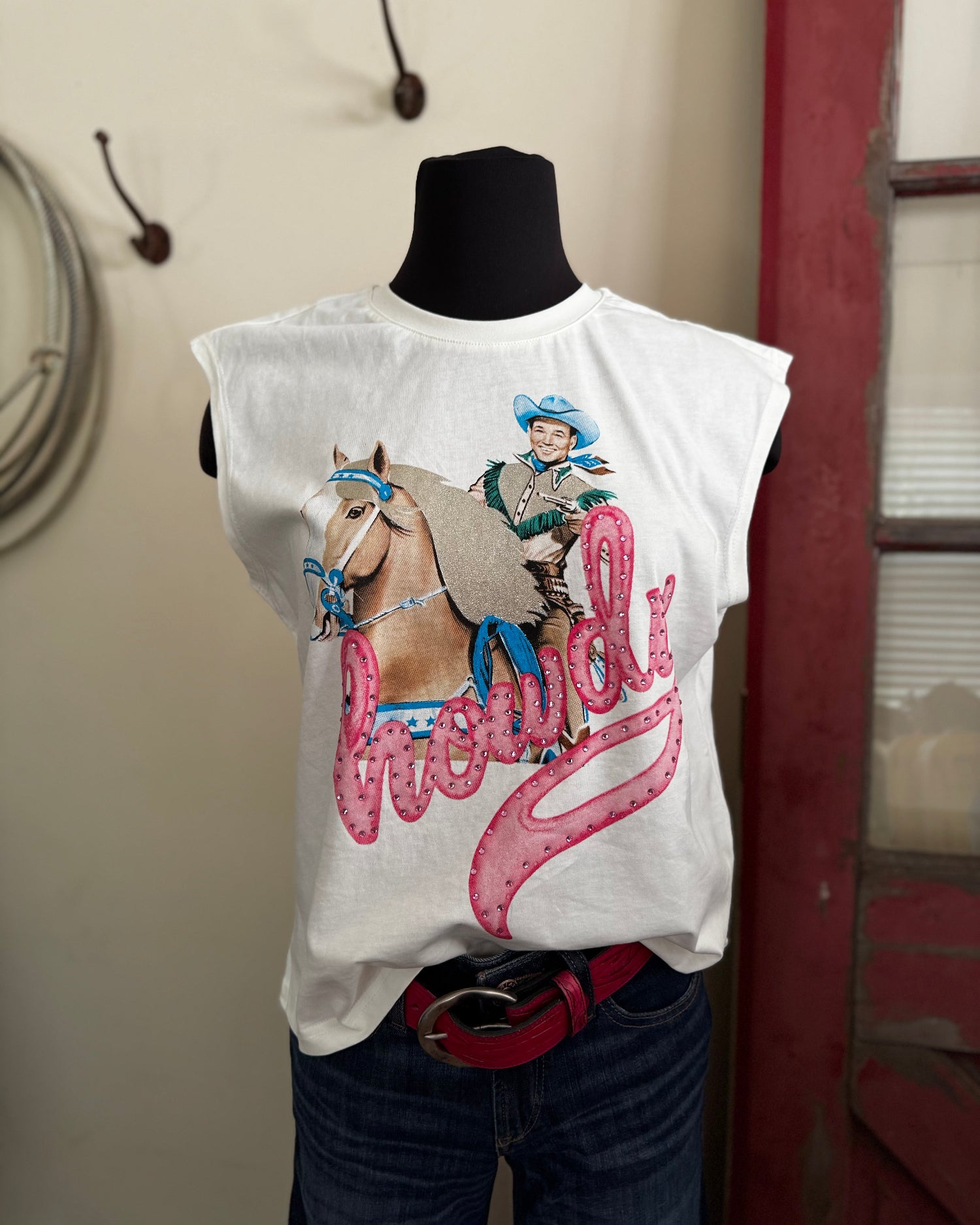 White sleeveless shirt with a graphic of a cowgirl on a horse and the word 'Chewy' displayed on a mannequin against a neutral wall.
