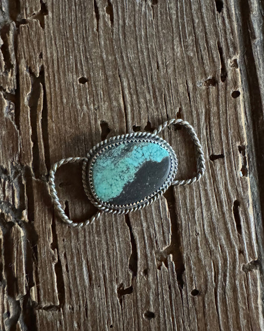 Silver twilly slide with a turquoise stone on a wooden surface