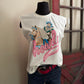 White sleeveless shirt with a graphic design of a cowboy and horse on a mannequin against a neutral wall.