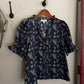 Navy floral blouse hanging on a wooden hanger against a white wall.