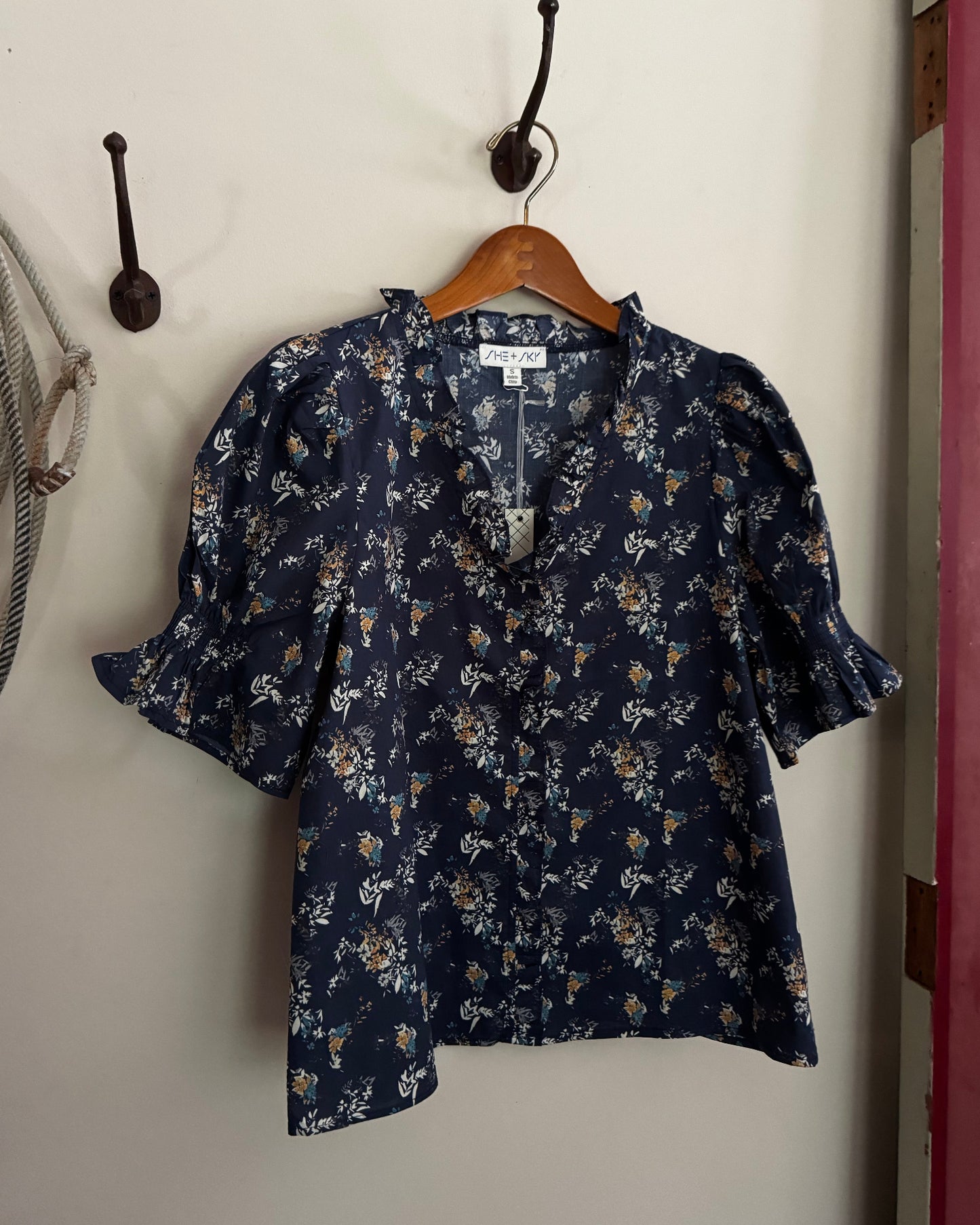Navy floral blouse hanging on a wooden hanger against a white wall.