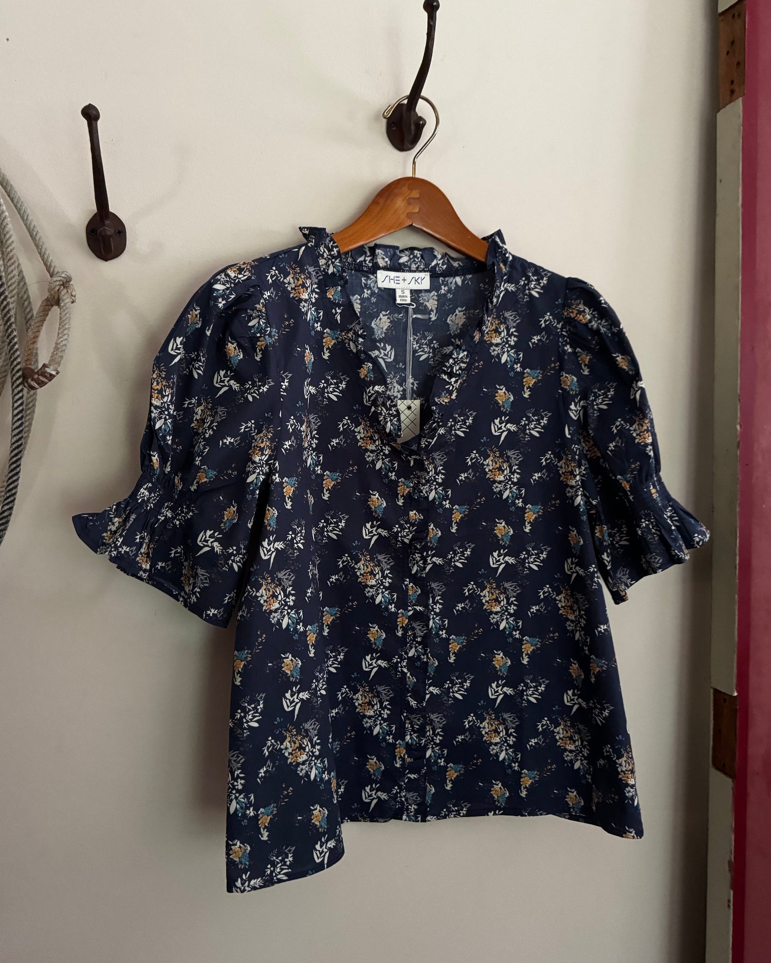 Navy floral blouse hanging on a wooden hanger against a white wall.