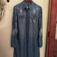 Blue denim shirt with cactus and moon designs on a hanger against a white wall.