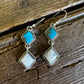 Pair of earrings with turquoise and white stones on a wooden surface