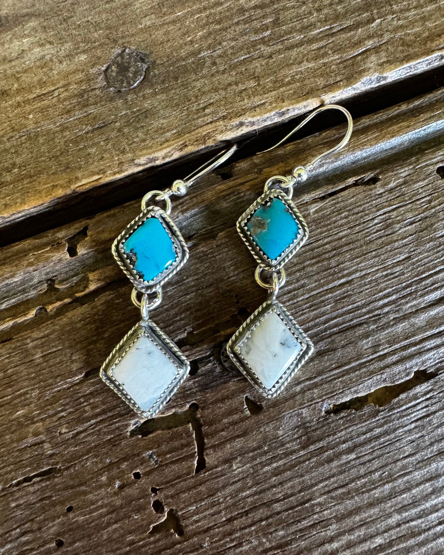Pair of earrings with turquoise and white stones on a wooden surface