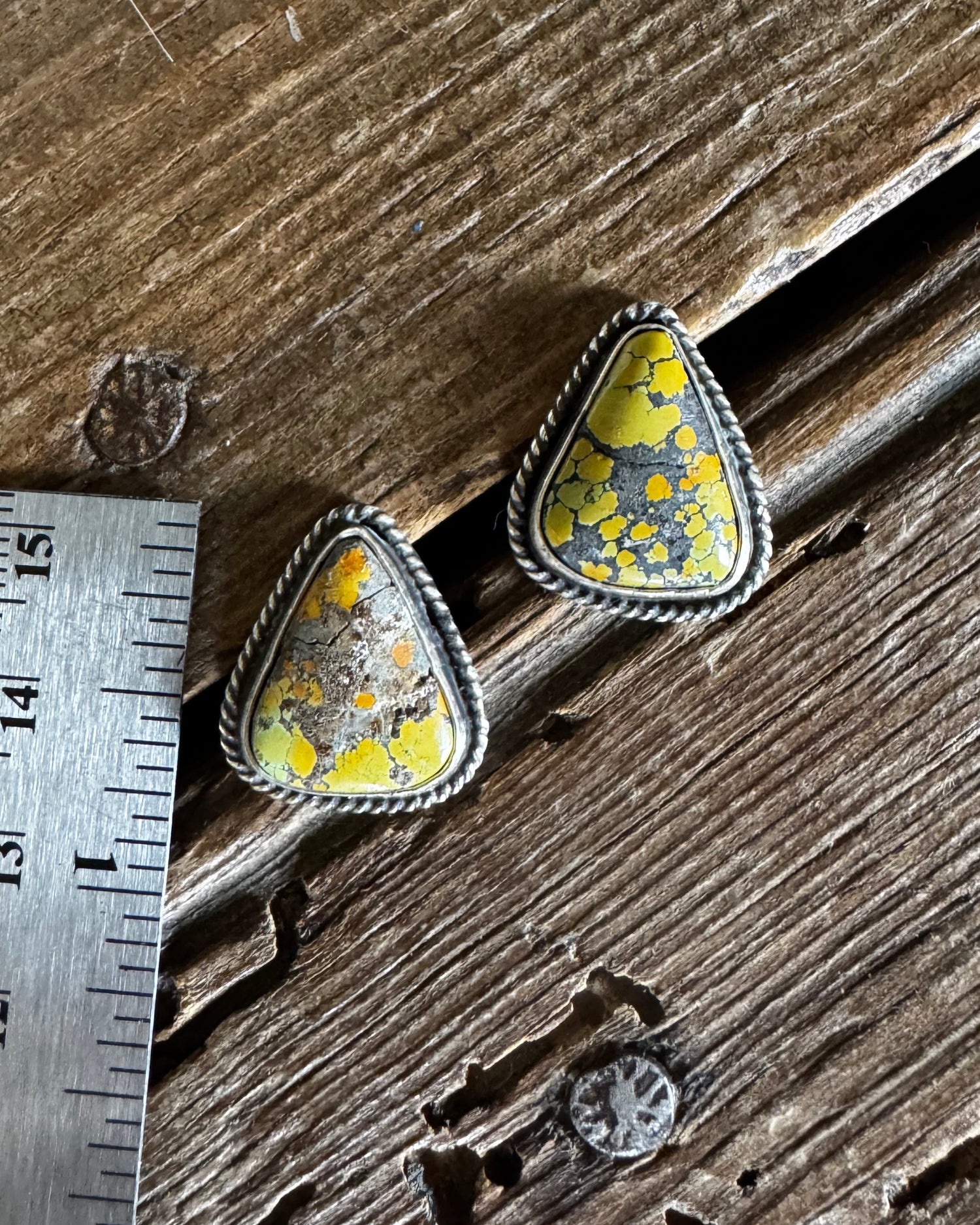 Pair of turquoise earrings on a wooden surface next to a ruler for scale