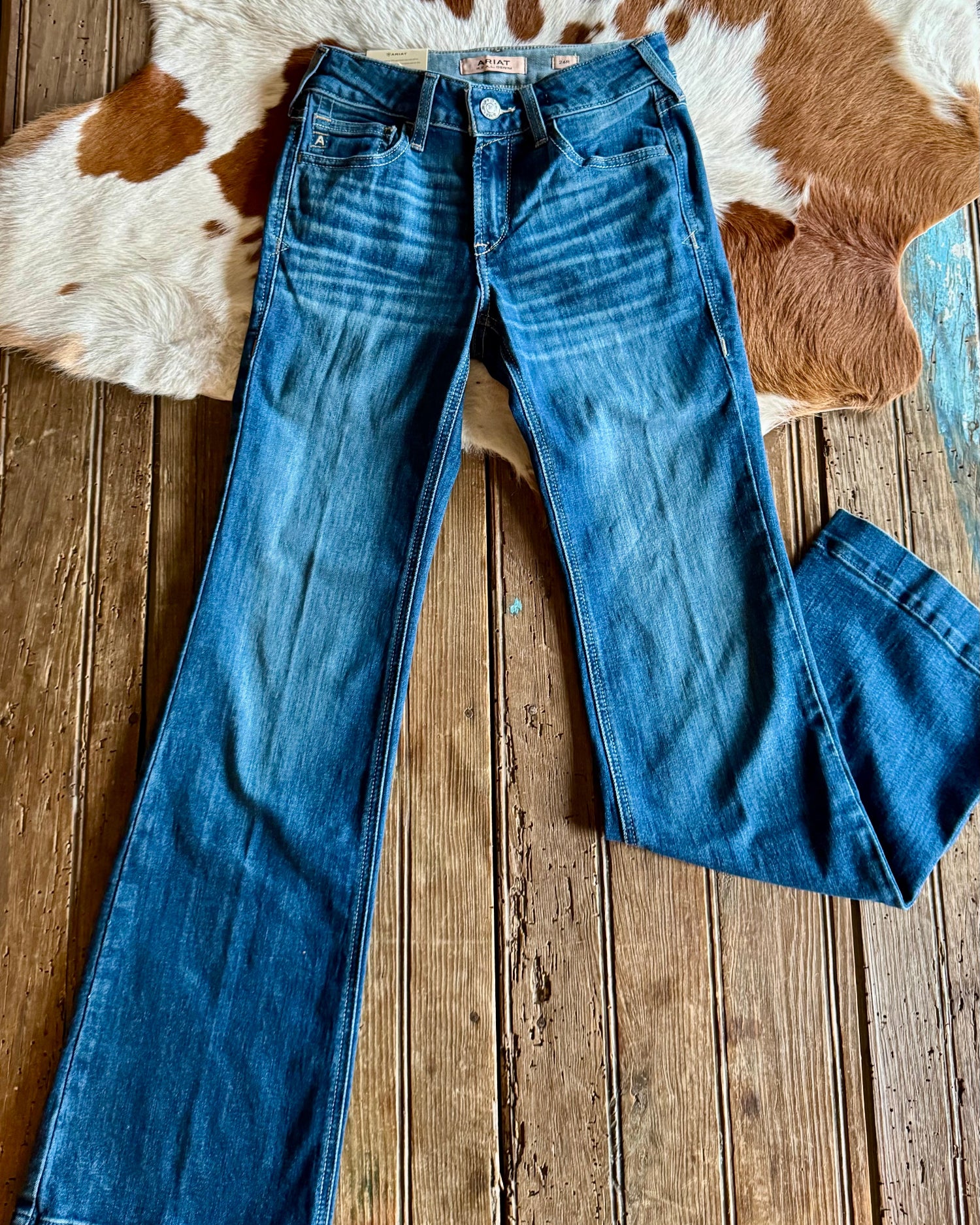 Blue jeans on a wooden floor with a cowhide rug in the background