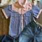 Blue and pink checkered shirt with floral collar on a wooden surface with jeans and a hat.