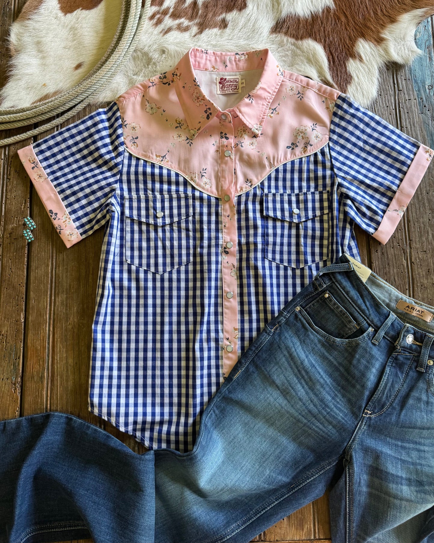 Blue and pink checkered shirt with floral collar on a wooden surface with jeans and a hat.
