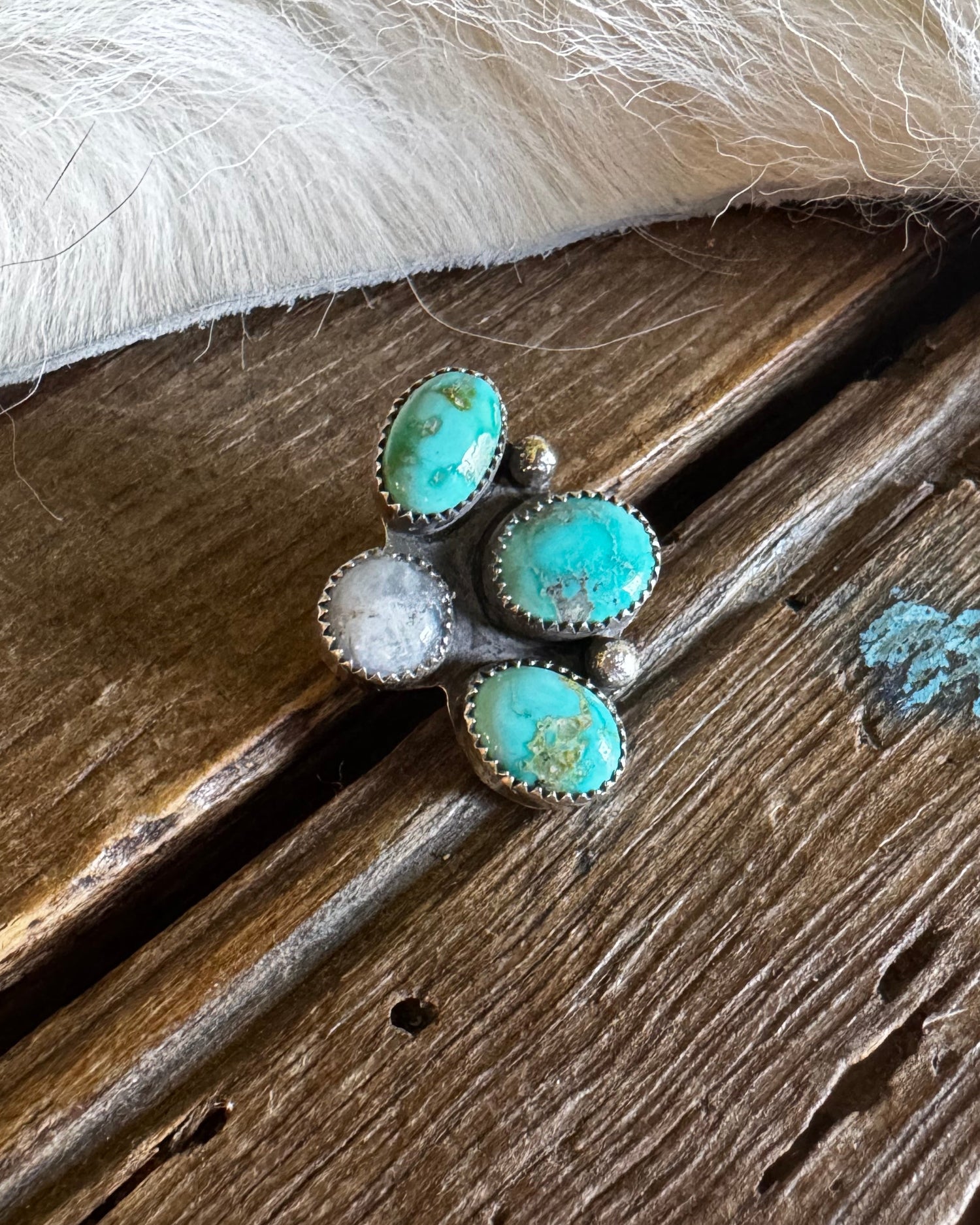 Turquoise stone ring on a wooden surface with white fur