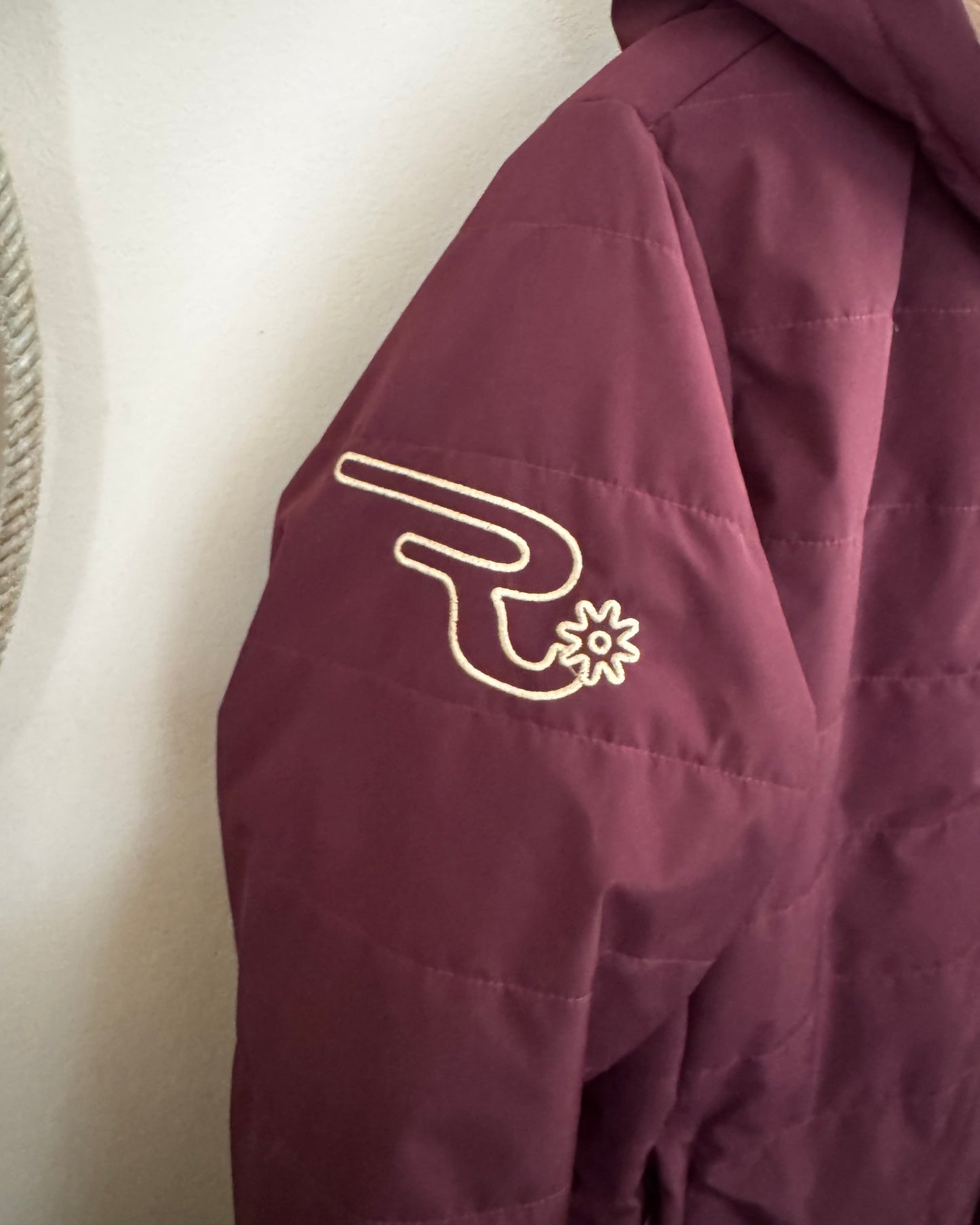 Close-up of a maroon jacket with a logo on a white background
