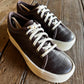 Pair of brown sneakers with white laces on a wooden surface