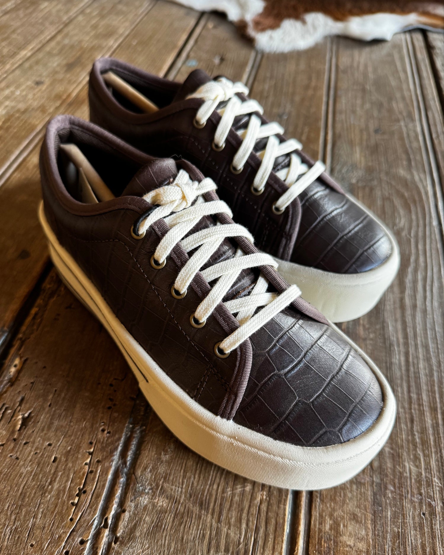 Pair of brown sneakers with white laces on a wooden surface