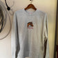 Sweatshirt with embroidered horse on a cream background with a rope and a door