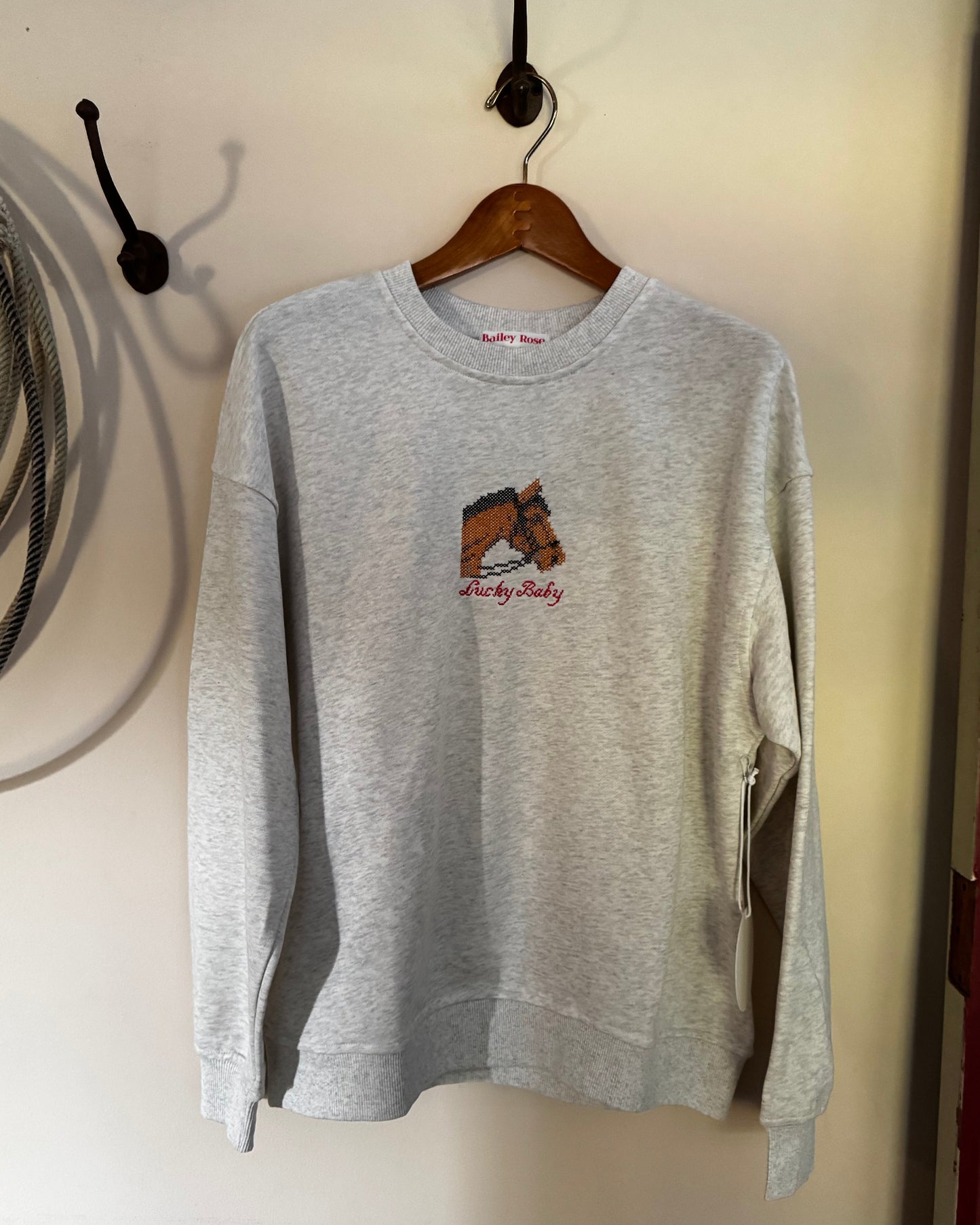 Sweatshirt with embroidered horse on a cream background with a rope and a door