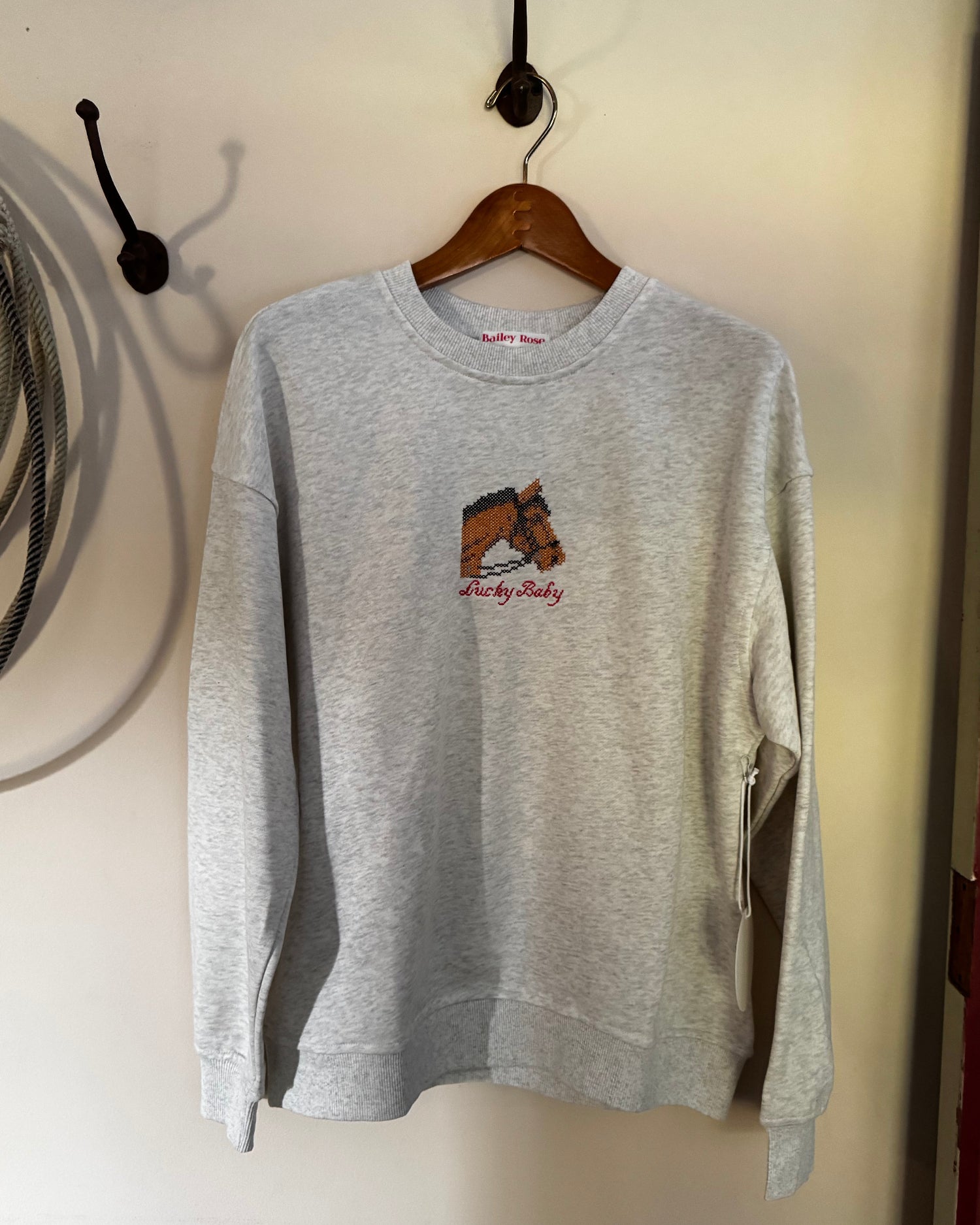 Sweatshirt with embroidered horse on a cream background with a rope and a door
