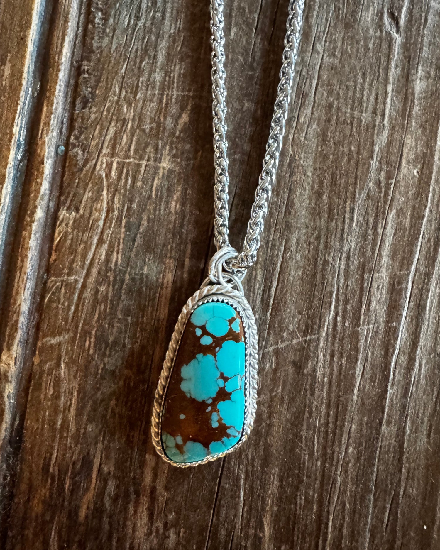 Turquoise stone pendant on a chain against a wooden background