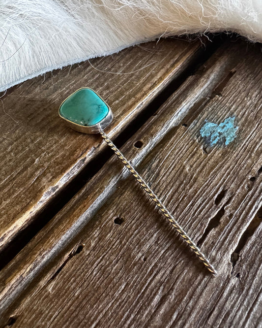 Turquoise stone pendant on a chain against a wooden surface