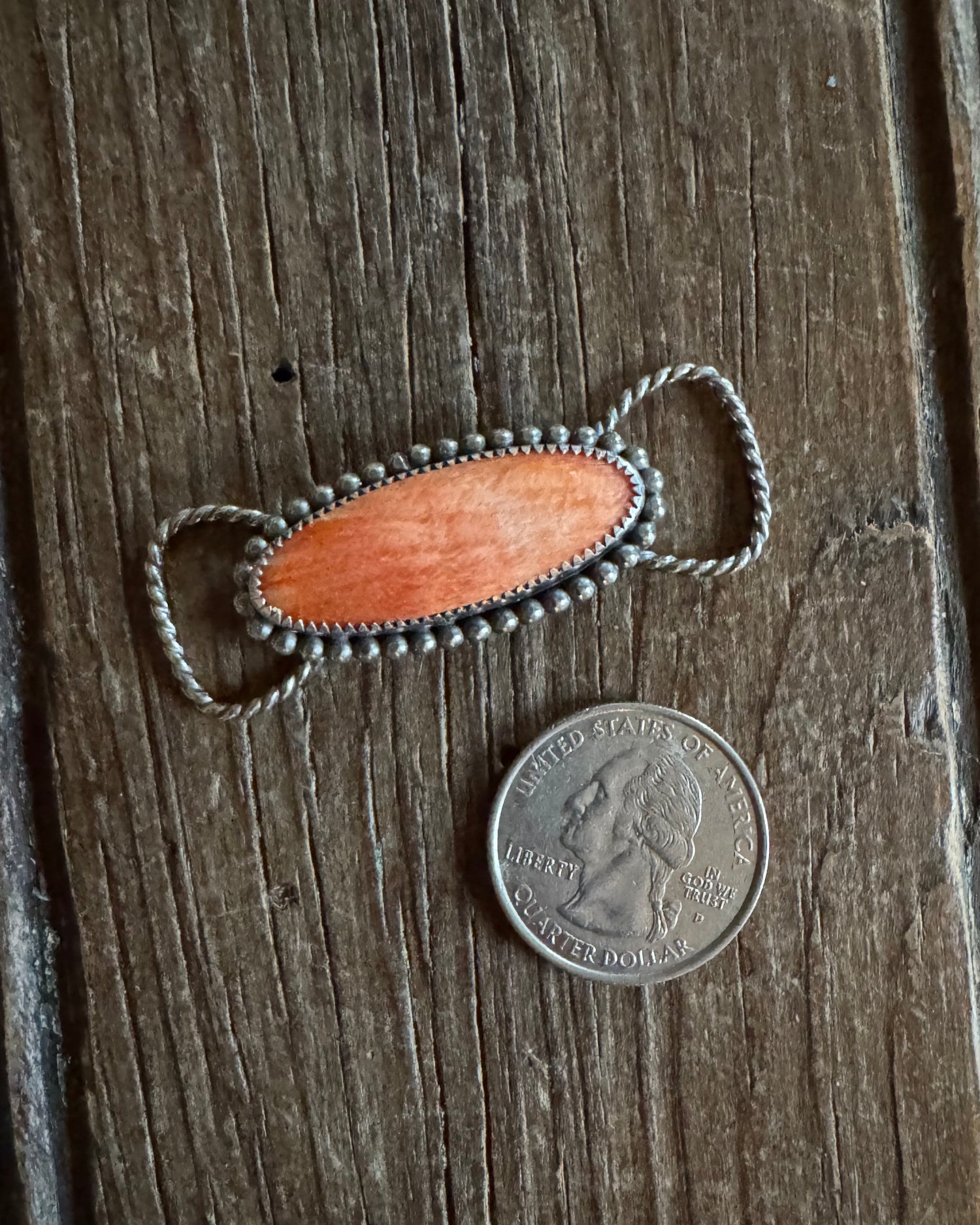 Decorative Twilly Slide with wooden center and metal accents on a wooden surface, next to a coin for scale.