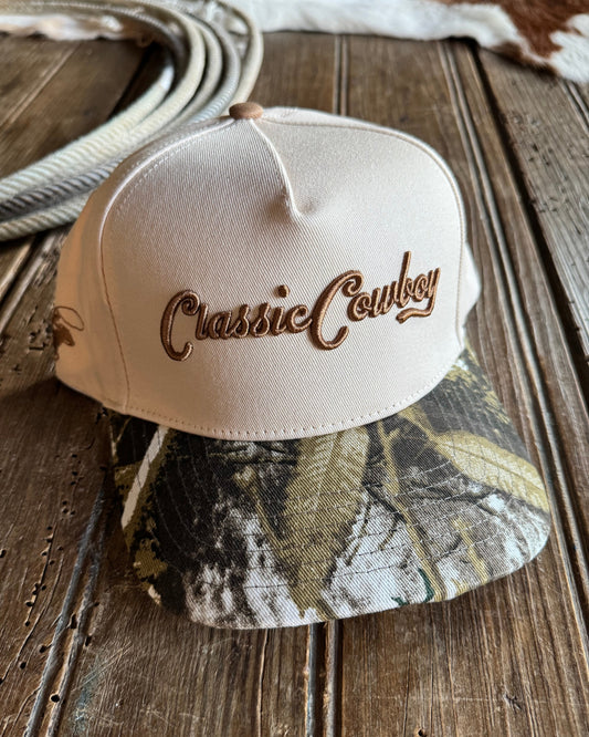 Beige and camouflage baseball caps with 'Classic Cowboy' branding on a wooden surface.