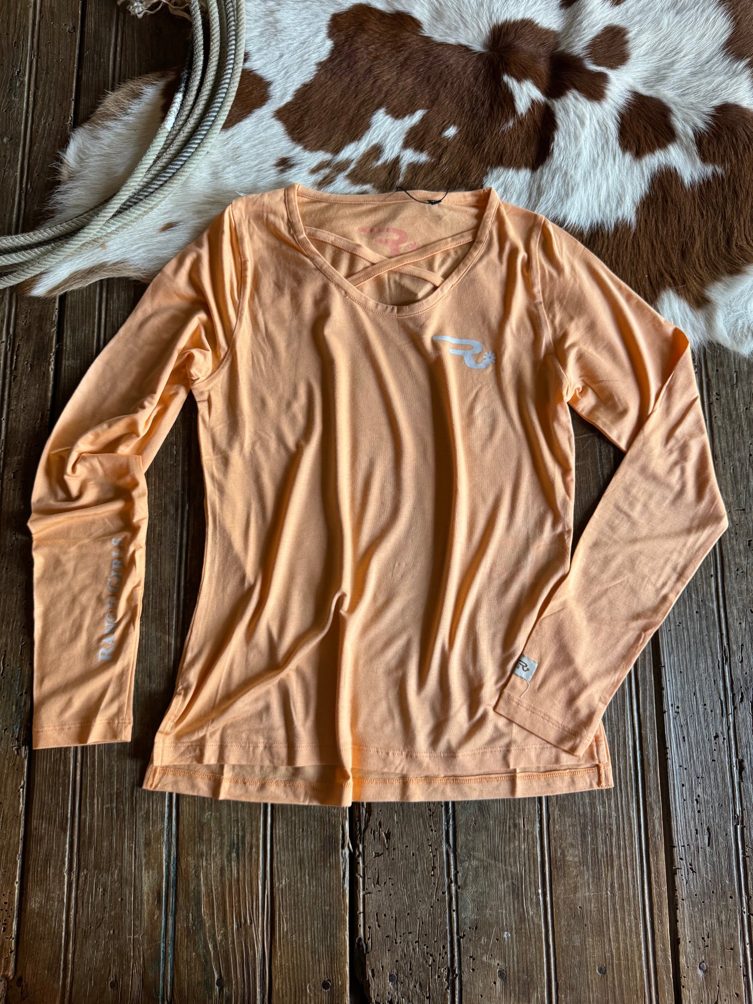 Beige t-shirt with logos on a wooden surface next to a cowhide rug
