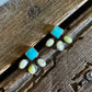 A pair of small silver-toned stud earrings with square turquoise-blue centers and oval milky-white stones, arranged on a rustic wooden surface with a white textured fabric at the top.