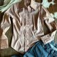 Light pink blouse with ruffled details on a wooden surface with denim pants.
