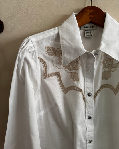 White shirt with floral embroidery on a hanger against a beige wall