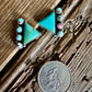 Turquoise triangle-shaped earrings on a wooden surface with a quarter for scale.