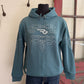 Blue hoodie with white patterns on a mannequin against a neutral wall.
