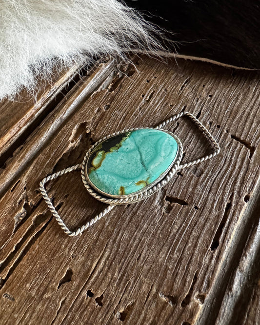 Turquoise stone pendant on a wooden surface with fur in the background