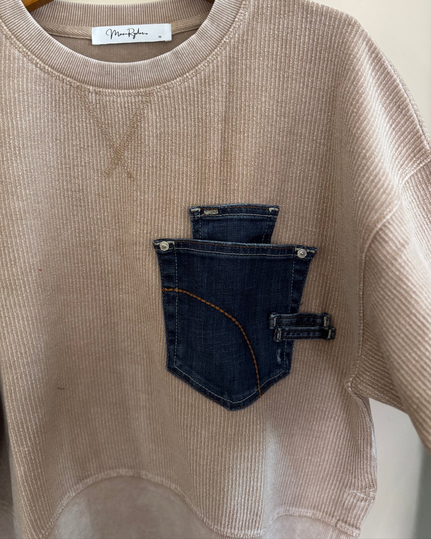 Beige ribbed sweater with a denim pocket on a hanger