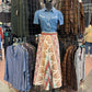 Mannequin wearing a blue shirt and patterned skirt in a clothing store setting.
