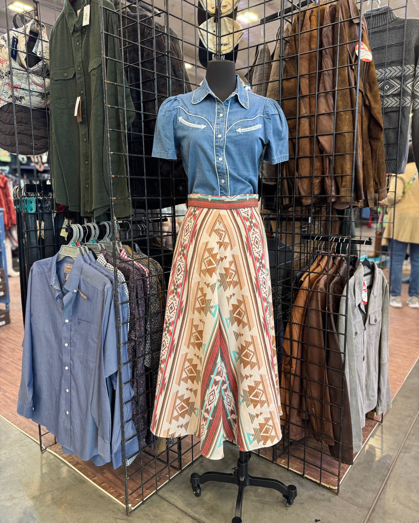 Mannequin wearing a blue shirt and patterned skirt in a clothing store setting.