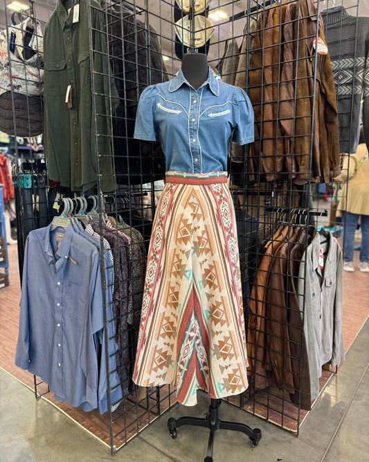 Mannequin wearing a blue shirt and patterned skirt in a clothing store setting.