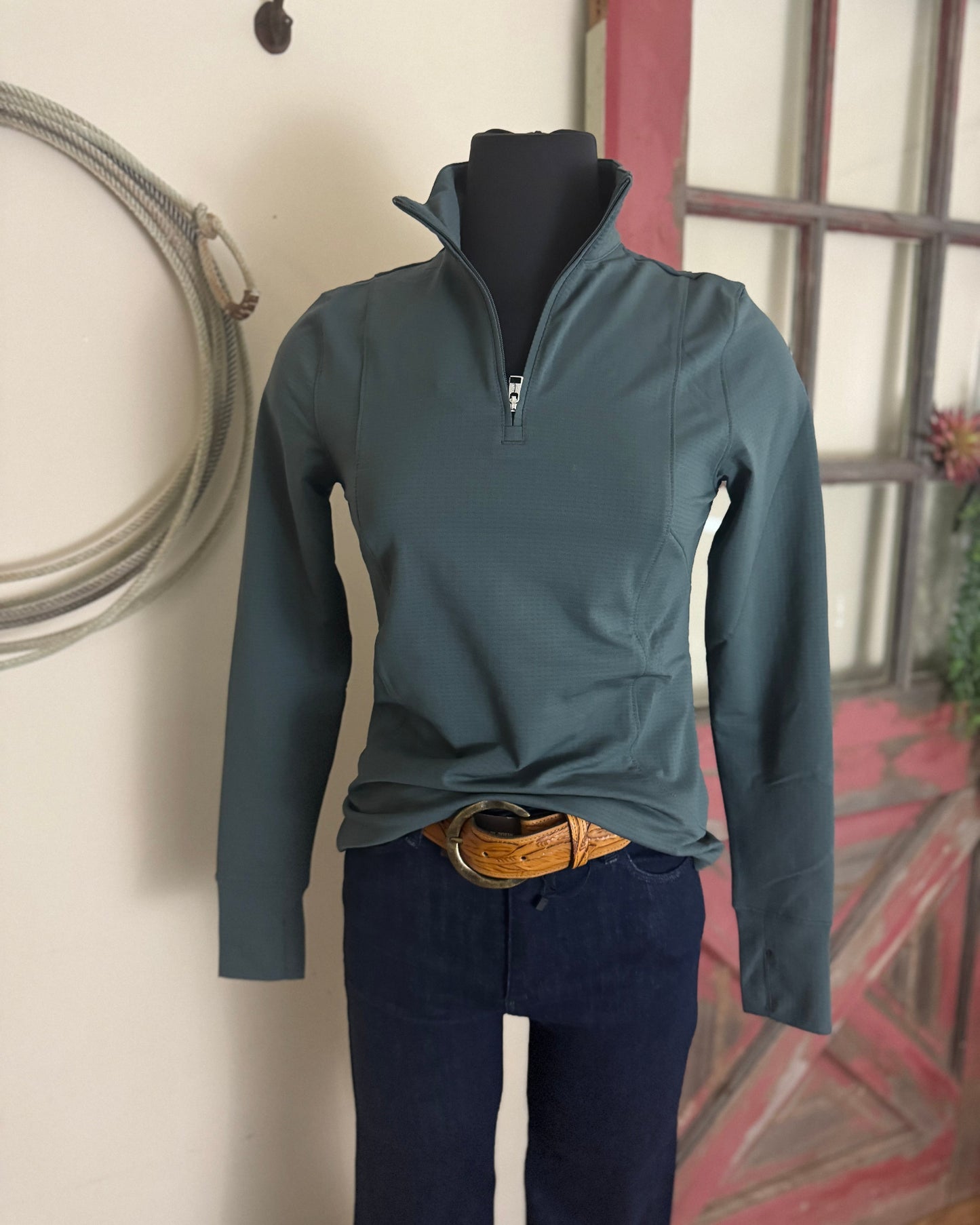 Mannequin wearing a teal long-sleeve shirt and dark pants against a neutral wall.