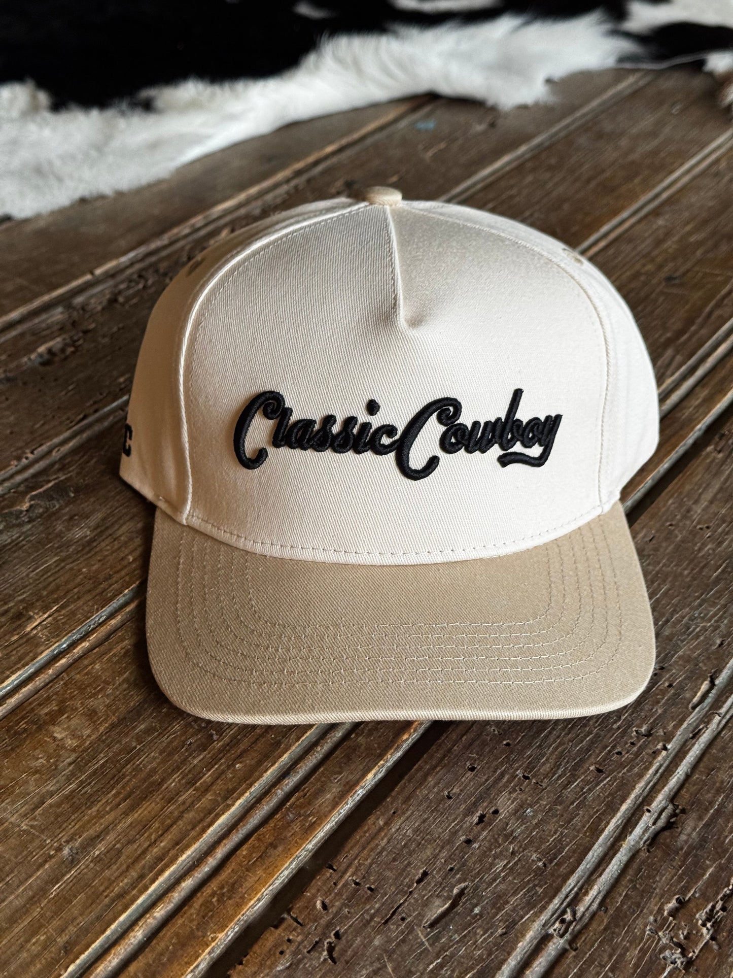 Beige cap with 'Casual Cowboy' text on a wooden surface
