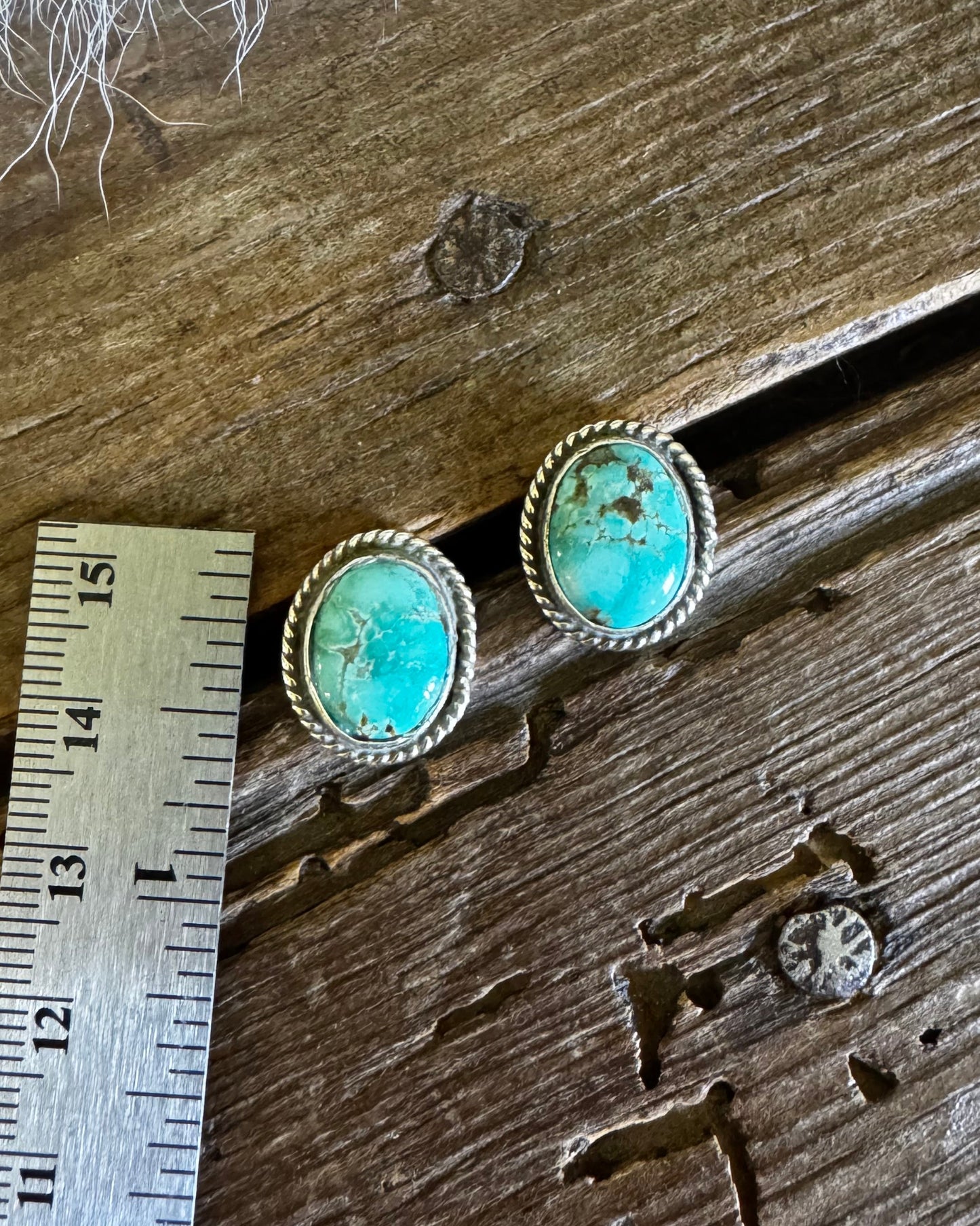 Turquoise earrings on a wooden surface with a ruler for scale.