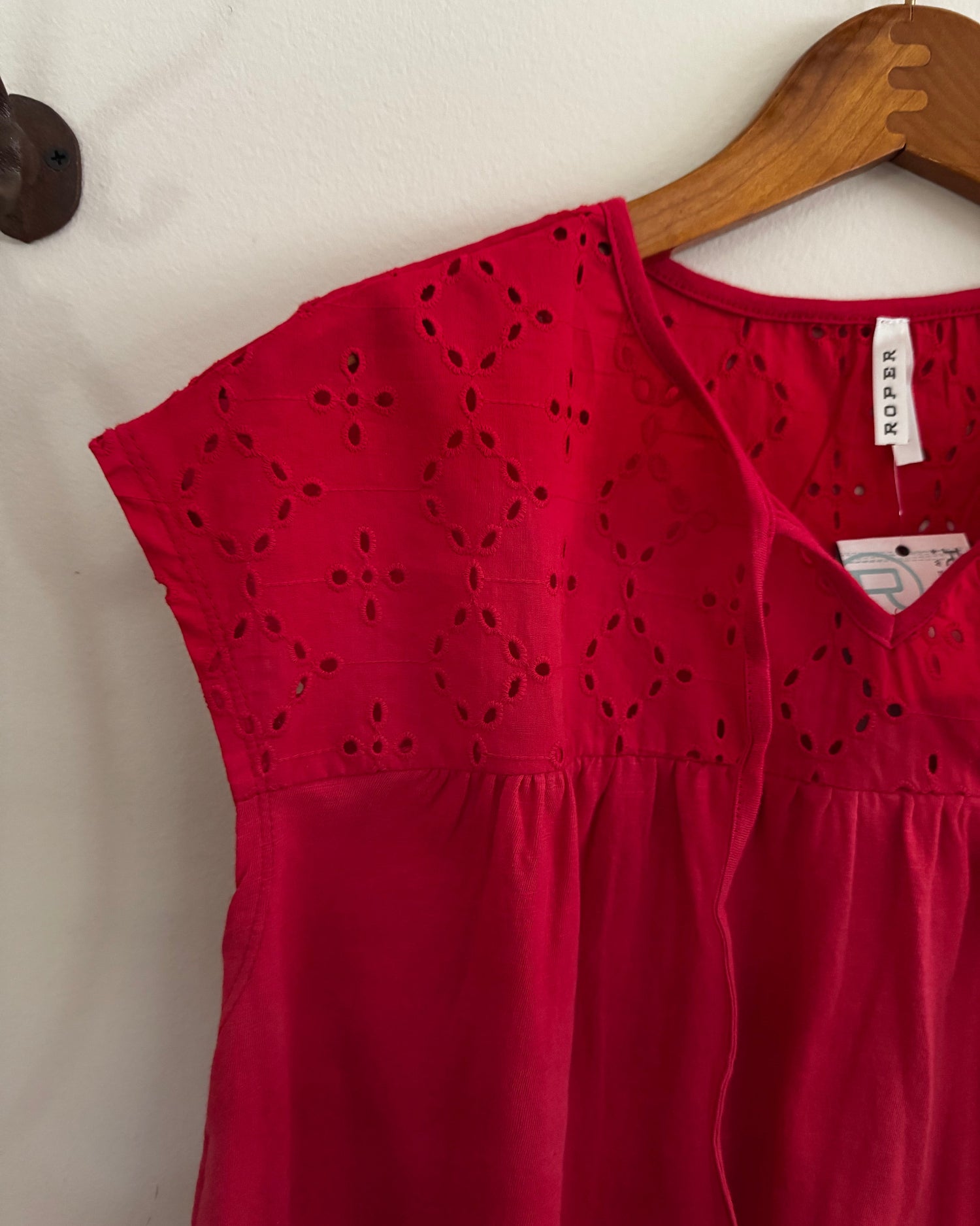 Red dress with cut-out details on a hanger against a white wall