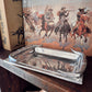 Silver tray on a wooden surface with a book featuring illustrations of cowboys in the background.
