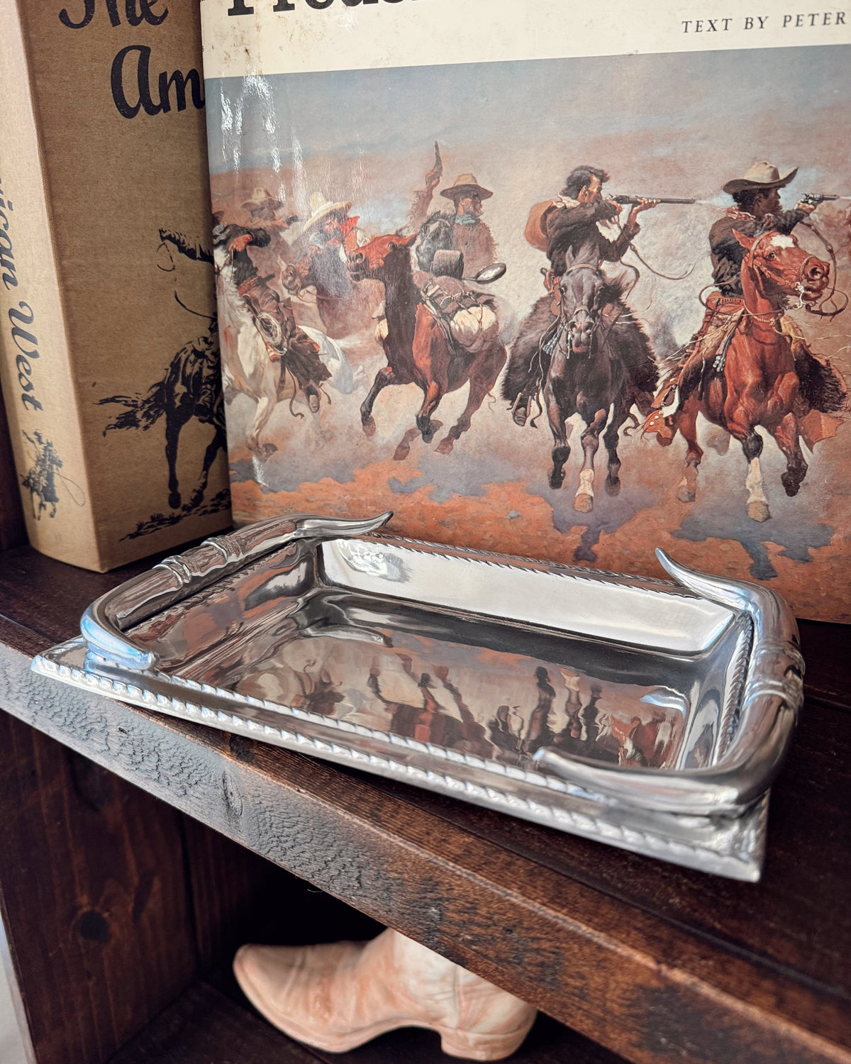 Silver tray on a wooden surface with a book featuring illustrations of cowboys in the background.
