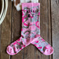 Pink and gray camouflage socks on a wooden surface with a cowhide rug and rope.