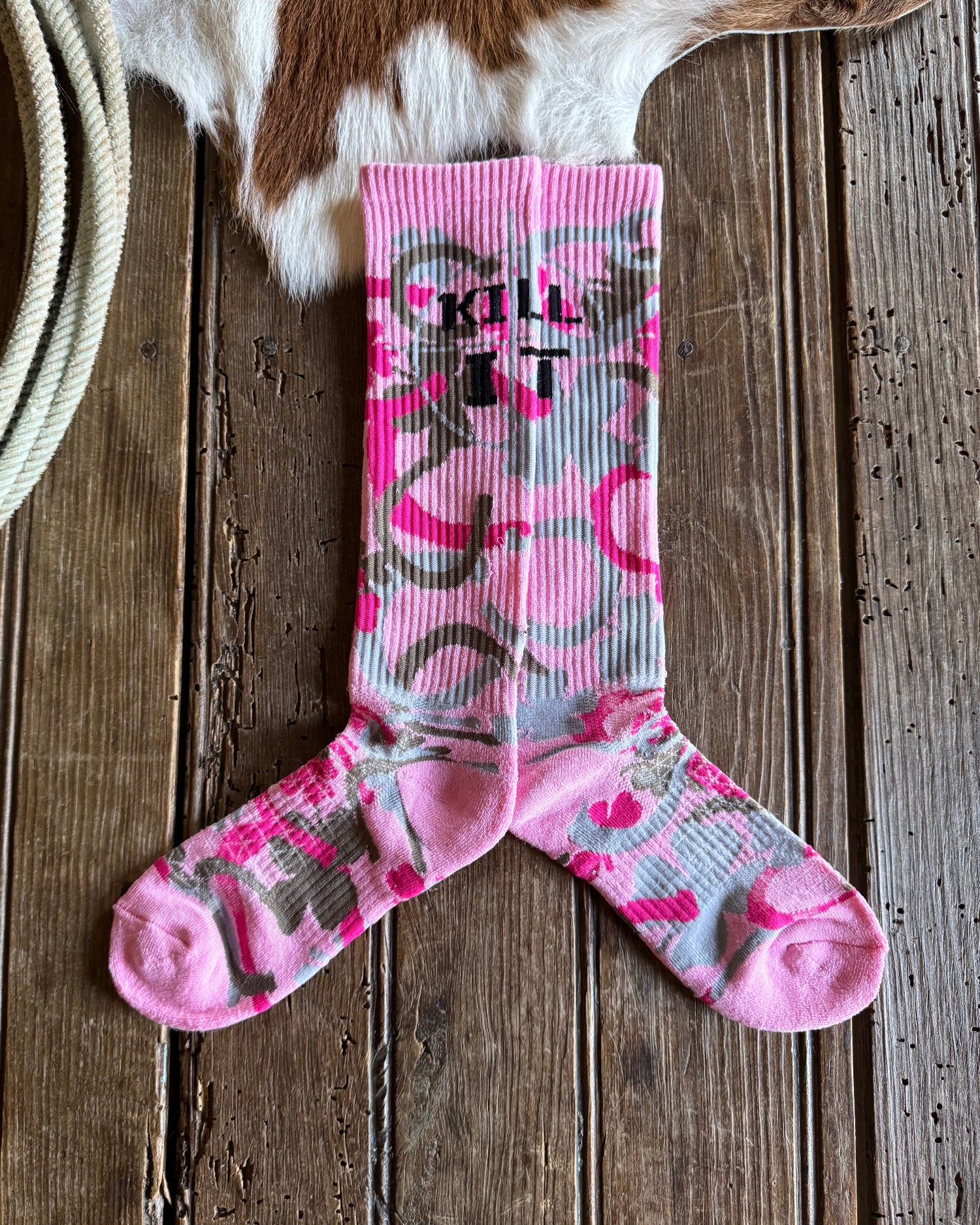 Pink and gray camouflage socks on a wooden surface with a cowhide rug and rope.