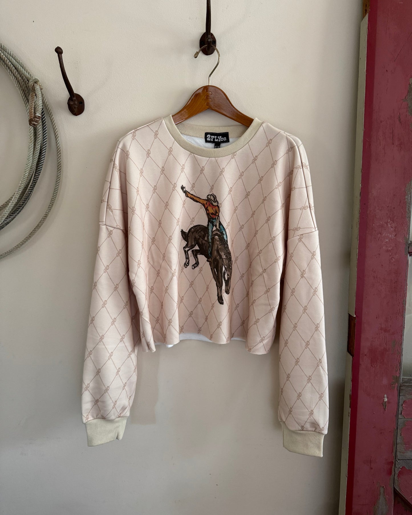Beige sweater with a logo on a hanger against a white wall.