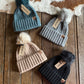 Four beanies with tags on a wooden surface next to a cowhide rug.
