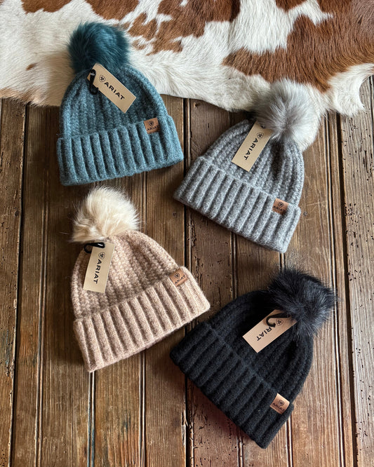 Four beanies with tags on a wooden surface next to a cowhide rug.