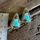 Turquoise stone earrings on a wooden surface with a ruler for scale.