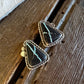 A pair of triangular black stone earrings with turquoise veining and gold-toned bezel settings, resting on a rustic wooden surface next to a white faux fur trim.